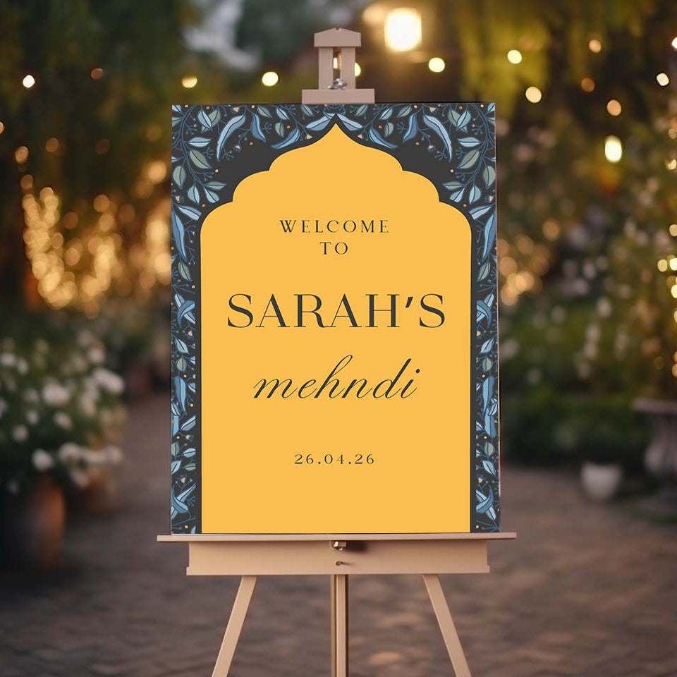 Decorative sign on an easel with 'Welcome to Sarah's mehndi' text against a blurred festive background.